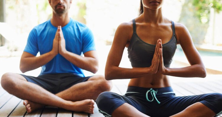 Two individuals practice yoga, sitting cross-legged with their hands in a prayer position, seeking inner peace.