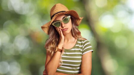 A person wearing shit-coloured sunglasses stands outdoor looking sad and unimpressed, hinting at the lingering effects of trauma and CPTSD.