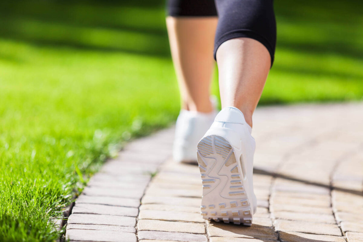 walking-meditation-feet-shoes-grass-path-1800-sm A person walks on a curved pathway bordered by green grass, evoking a sense of calm that reflects the effects of walking meditation, taming your mind through presence and movement.