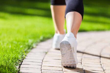 A person walks on a curved pathway bordered by green grass, evoking a sense of calm that reflects the effects of walking meditation, taming your mind through presence and movement.