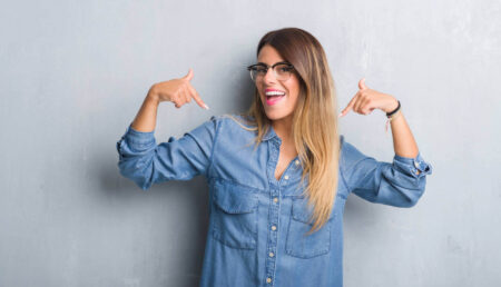 A woman smiles and points at herself with both hands, radiating self-confidence, enjoying being full of herself.