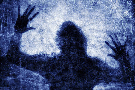 A dark, shadowy human figure presses their hands against a textured, scratched blue surface, evoking the silent struggles surrounding emotional abuse.