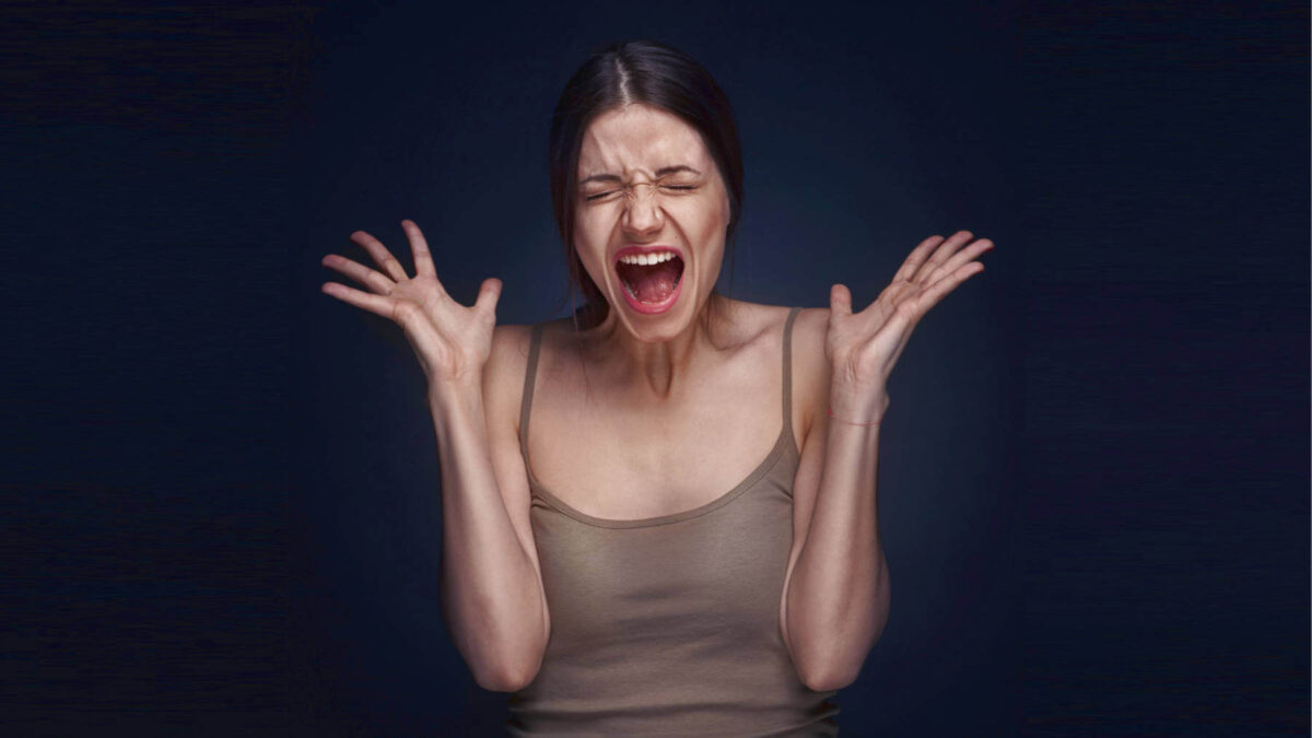 A woman is screaming with her eyes closed and hands raised, showing the courage to feel emotions.