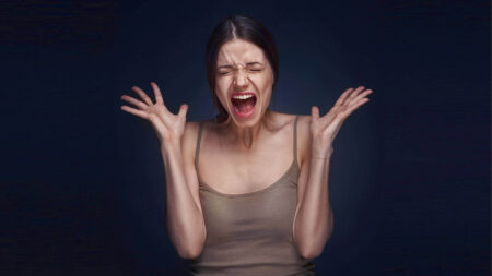 A woman is screaming with her eyes closed and hands raised, showing the courage to feel emotions.